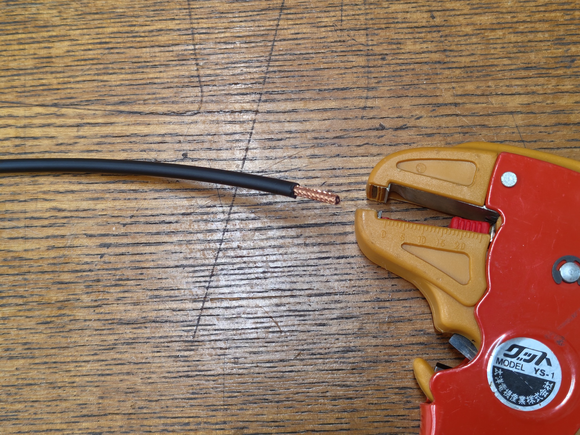 Image of cable end. The sheath is stripped about 15mm, leaving the part inside the shield wire (the tubular metal part). An orange cable stripper is placed on the right.